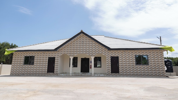 A building with a patterned facade, a pitched roof, and a small porch with columns.