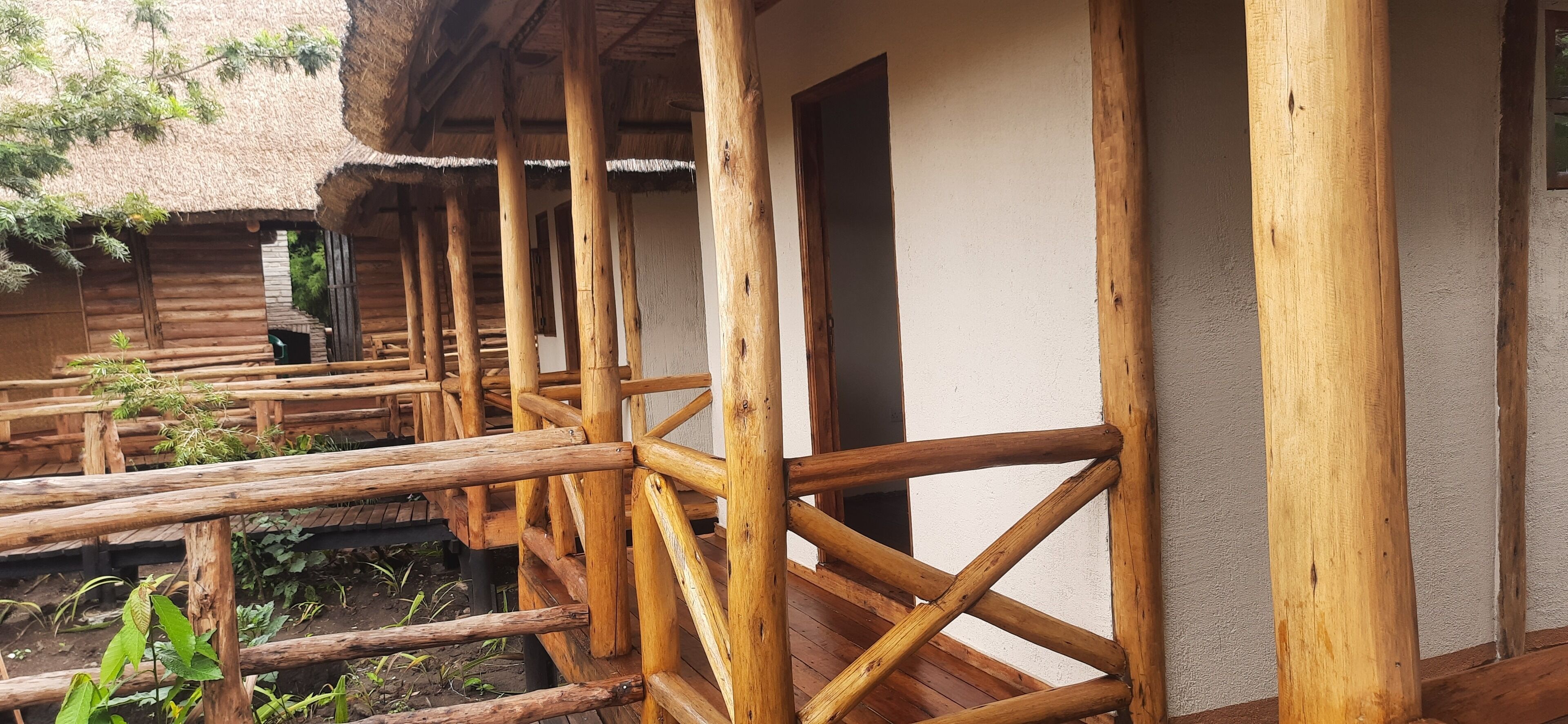 A wooden deck with a thatched roof structure, wooden railings, and a white wall.