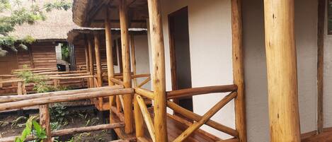 A wooden deck with a thatched roof structure, wooden railings, and a white wall.