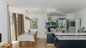 A modern kitchen with a central island, built-in appliances, and a dining area with a white tablecloth. - DiamondVilla, 4 bedroom Apartment, garden & spa (Hlavní mesto Praha)