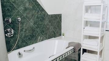 Une salle de bain moderne avec une baignoire blanche, un mur de douche recouvert de carreaux verts et un porte-serviettes blanc.