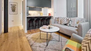A modern living room with a grey sofa, a round coffee table, and a kitchen area with bar stools. - Chic Two-bedroom Haven (Manchester)
