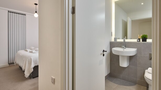 A modern bathroom with a white sink, a mirror, and a toilet. - Chic Two-bedroom Haven (Manchester)