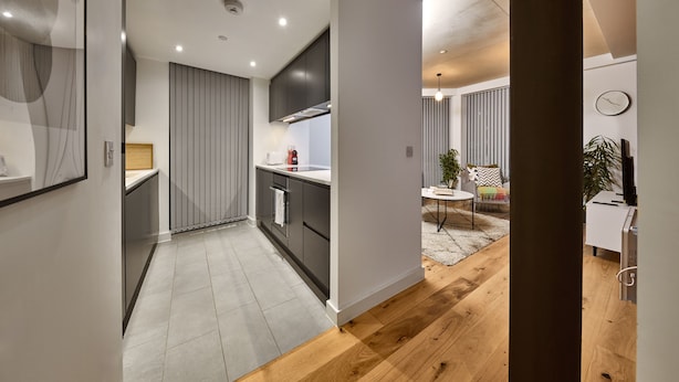 A modern kitchen with dark cabinets, a white countertop, and a wooden floor. - Chic Two-bedroom Haven (Manchester)
