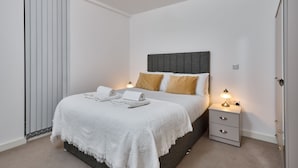 A neatly arranged bedroom with a bed, bedside lamps, a nightstand, and a wardrobe. - Chic Two-bedroom Haven (Manchester)