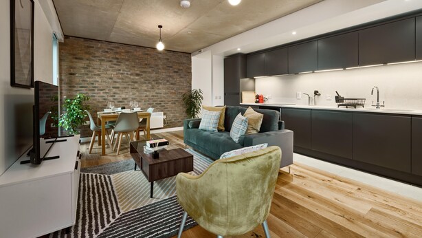 Ein modernes Wohnzimmer mit Essbereich, einem grauen Sofa, einem Holztisch und einem Fernseher auf einem weißen Lowboard.