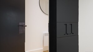Ein Zimmer mit einer dunklen Tür, einer weißen Wand, einem runden Spiegel und einer weißen Heizung.