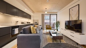 Eine moderne Küche mit dunklen Schränken, ein graues Sofa und ein Fernseher in einem Wohnbereich mit großem Fenster.