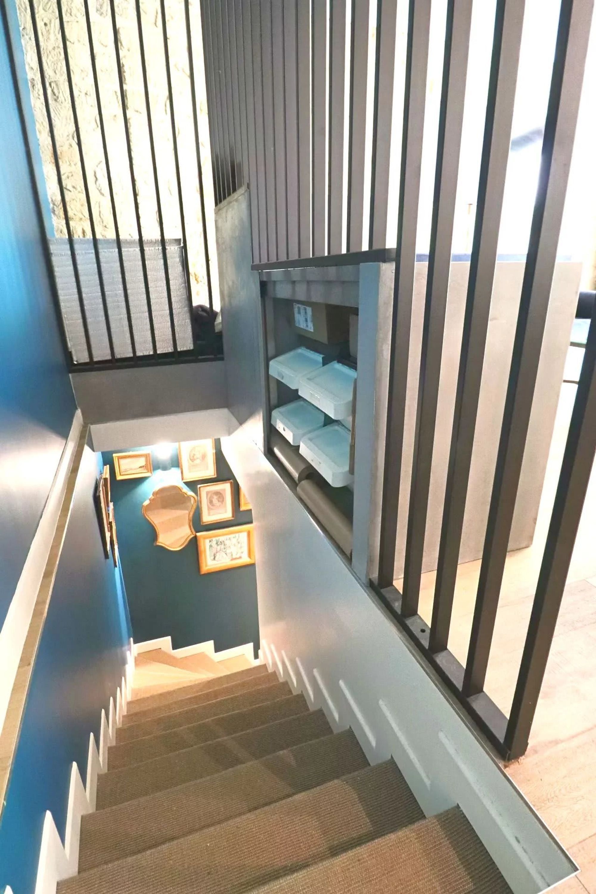 A staircase with a blue wall, a wooden handrail, and framed pictures on the landing.