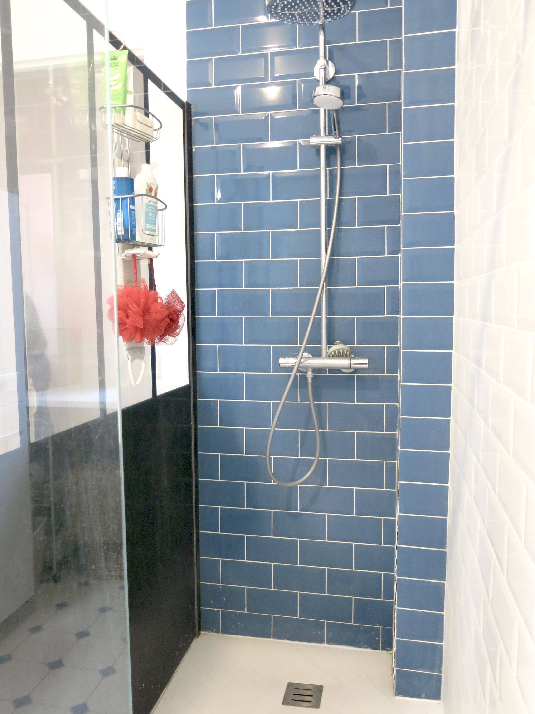 A bathroom with blue tiled walls, a shower with a handheld showerhead, and a glass shower door.