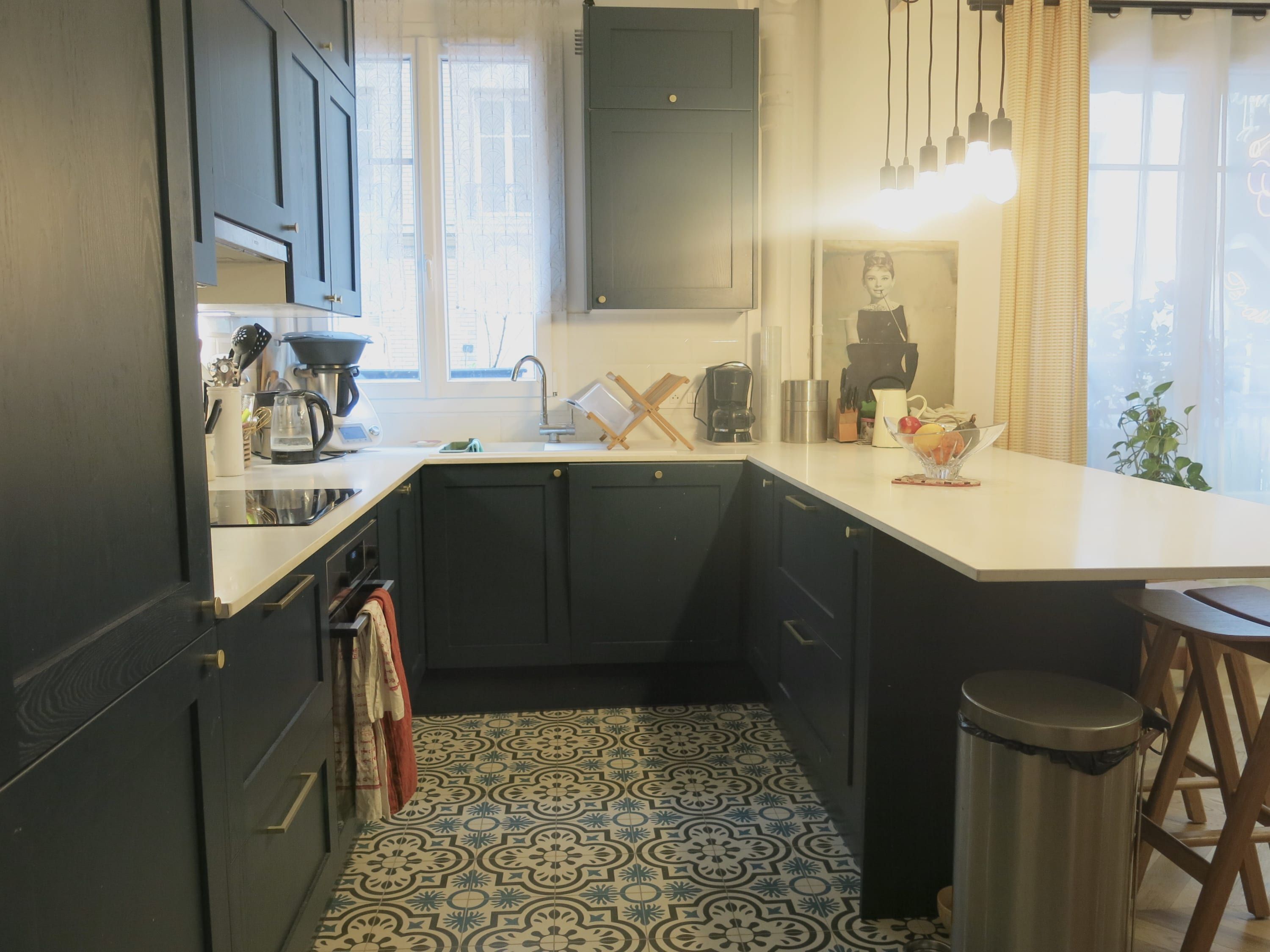 A kitchen with dark cabinets, a white countertop, a patterned floor, and a hanging light fixture.