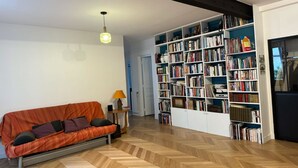 A living room with a sofa, a bookshelf, and a herringbone-patterned floor. - Appartement Village Daguerre Citycosy (Paris)