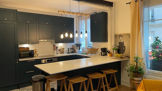 A modern kitchen with dark cabinets, a white island, and bar stools. - Appartement Village Daguerre Citycosy (Paris)