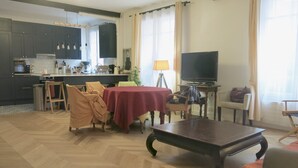 A living room with a dining table, chairs, a TV, and a kitchen in the background. - Appartement Village Daguerre Citycosy (Paris)