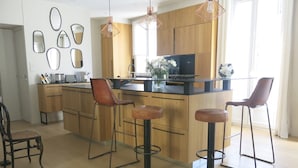 Une cuisine moderne avec des meubles en bois, un îlot central doté de tabourets, un éclairage suspendu et une grande fenêtre qui laisse entrer la lumière naturelle.