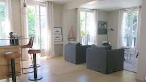 Un vaste espace de vie comprenant un bar, deux canapés gris et une table à manger.