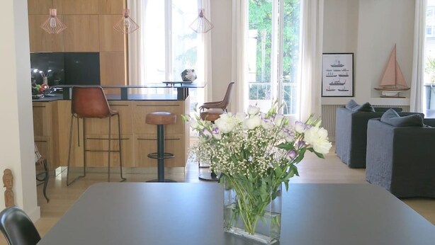 Un espace de salle à manger moderne avec une longue table, un vase de fleurs et une cuisine en arrière-plan.