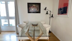 A modern dining area with a glass-top table, white chairs, a framed painting, and a floor lamp. - Appartement Grand Veneur Citycosy (Paris)