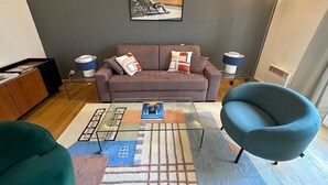 A modern living room with a grey sofa, a glass coffee table, a blue armchair, and a framed picture on the wall. - Appartement Grand Veneur Citycosy (Paris)