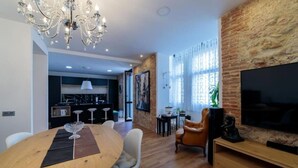 Un soggiorno moderno con zona pranzo, cucina sullo sfondo e televisore montato su una parete in mattoni.