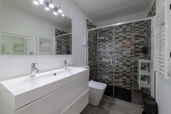 A modern bathroom with a large white sink, a mirror, and a glass-enclosed shower.