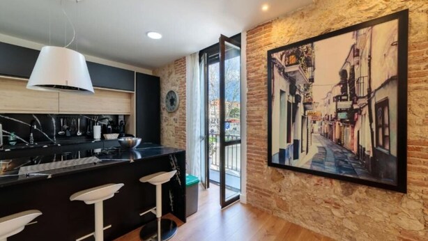Una cucina moderna con isola nera, sgabelli da bar bianchi e un'ampia finestra che si affaccia su una strada.