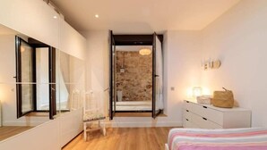 Una camera da letto moderna con un letto grande, un comodino, un armadio e un bagno visibile attraverso una porta aperta.