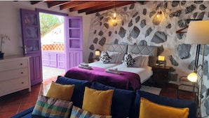 A bedroom with a stone wall, a bed with a headboard, a dresser, and a window with purple shutters. - Los Cerrajones: spectacular views from the cliff (Agulo)