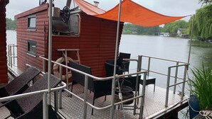 A wooden cabin with a metal deck, outdoor seating, and a view of the water. - Small houseboat ideal for fishing.   Contact us +49 177 5927586 (Lychen)