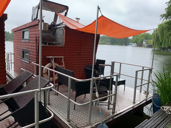A wooden cabin with a metal deck, outdoor seating, and a view of the water.