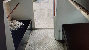 A room with a patterned floor, a bed with a dark headboard, a small table with a decorative item, and a window with a view of a building. - Small houseboat ideal for fishing.   Contact us +49 177 5927586 (Lychen)