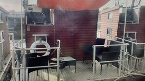 A covered outdoor area with a red canopy, metal railings, and a table with chairs. - Small houseboat ideal for fishing.   Contact us +49 177 5927586 (Lychen)