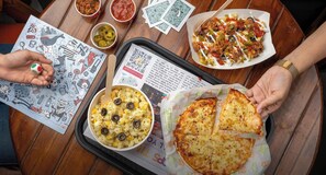 A tray with food items including a pizza, pasta, and a salad, along with a QR code and a menu on a wooden table. - goSTOPS Srinagar (Srinagar)