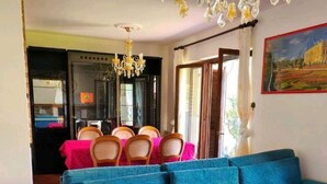 A living room with a blue sofa, a chandelier, and a dining area with a pink tablecloth. - LA VILLETTA (Piemonte)