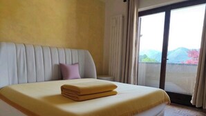 A hotel room with a large bed, a view through a sliding door, and a window with curtains. - LA VILLETTA (Piemonte)