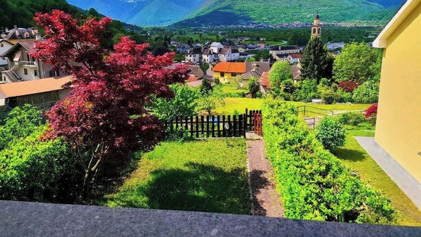 A town with a church, a mountain in the background, and a red flowering tree in the foreground. - LA VILLETTA (Piemonte)