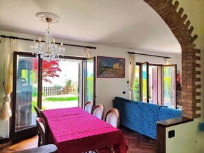 A dining area with a table and chairs, a chandelier, and a view through large windows. - LA VILLETTA (Piemonte)