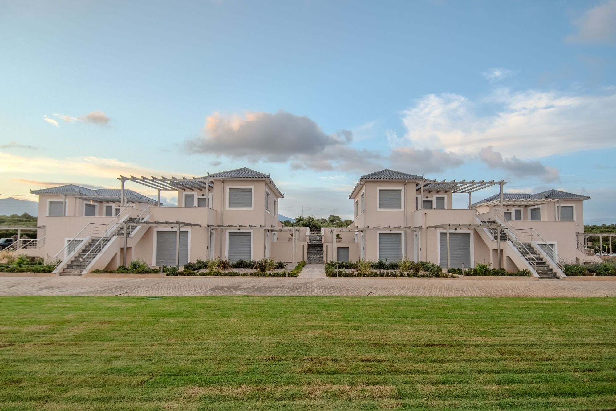 A modern two-story building with a symmetrical design, featuring a central staircase and a covered outdoor area with pergolas.