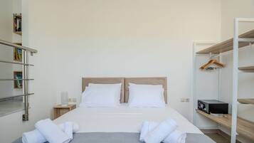 Een netjes opgemaakt bed met witte lakens en handdoeken, een nachtkastje met een lamp, en een kledingkast met daarin hangende kleding.
