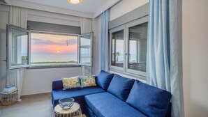 Un salon moderne avec un canapé bleu, une petite table ronde et une vue sur le coucher de soleil sur la mer.
