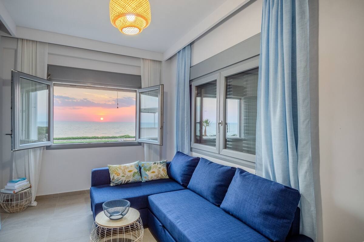 A modern living room with a blue sofa, a small round table, and a view of the sunset over the sea.