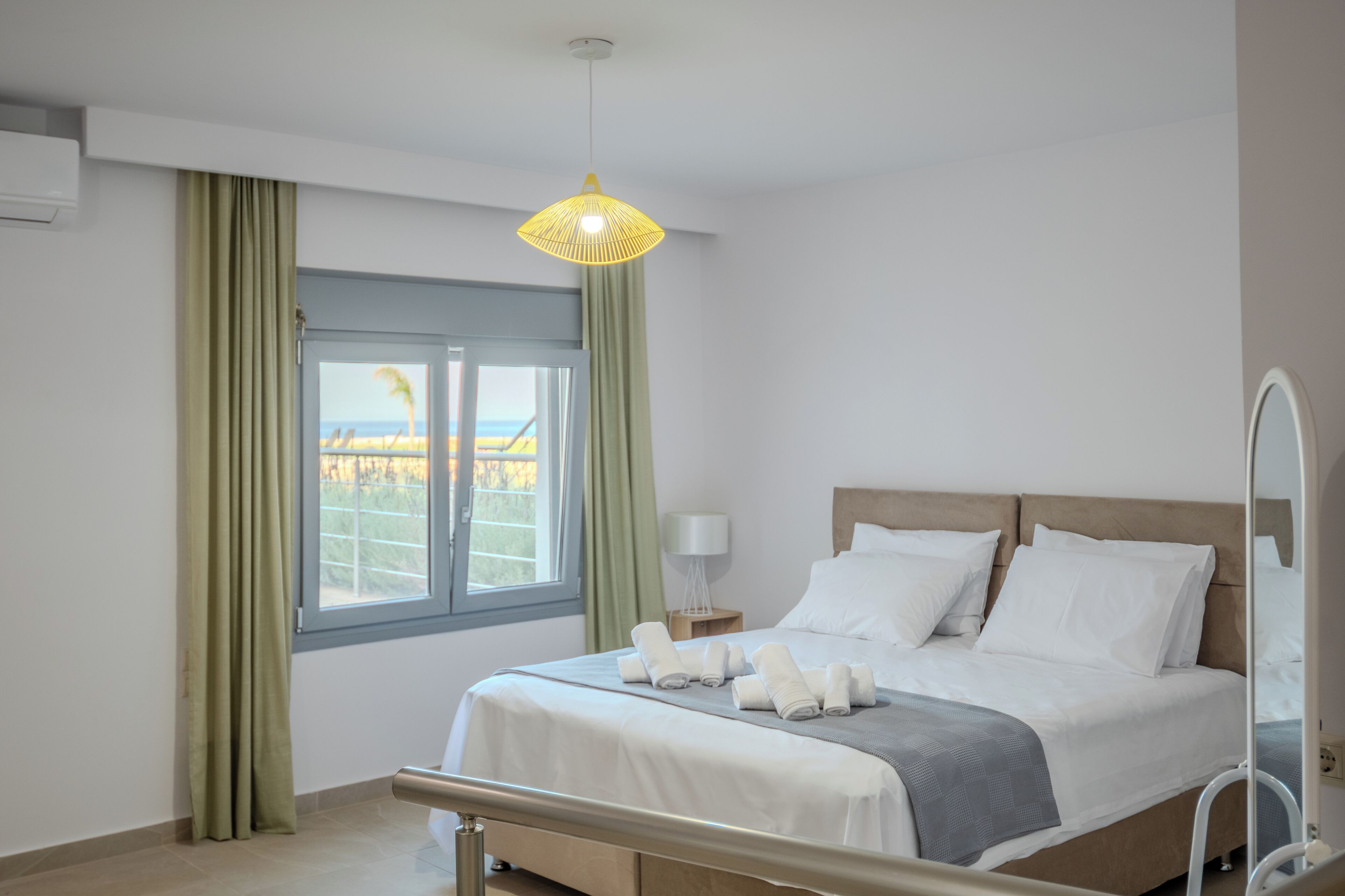Quarto de hotel moderno com cama, mesa de cabeceira, luminária e janela com cortinas.