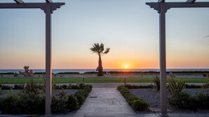 Un sentier menant à une plage offrant une vue sur le coucher de soleil, avec des palmiers et une sculpture rocheuse.