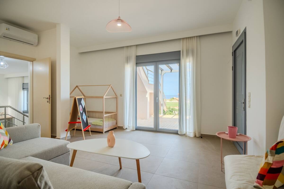 A modern living room with a sofa, a small table, a playhouse, and a view of the outdoors.