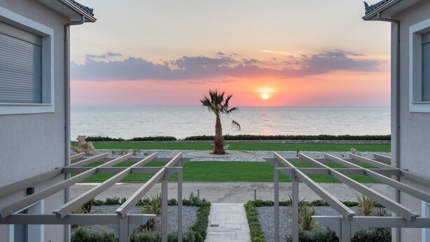 Un balcon offrant une vue sur le coucher de soleil sur la mer, un palmier et un sentier menant à la plage.