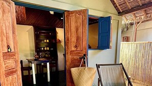 A wooden deck with a chair and a hanging basket, a Buddha statue, and a wooden door leading to a room with a blue interior. - Comfortable Malagasy bungalow on private beach (Analanjirofo)