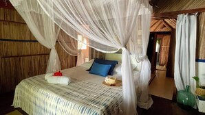 A room with a bed under a canopy, wooden walls, and a visible door leading to another room. - Comfortable Malagasy bungalow on private beach (Analanjirofo)