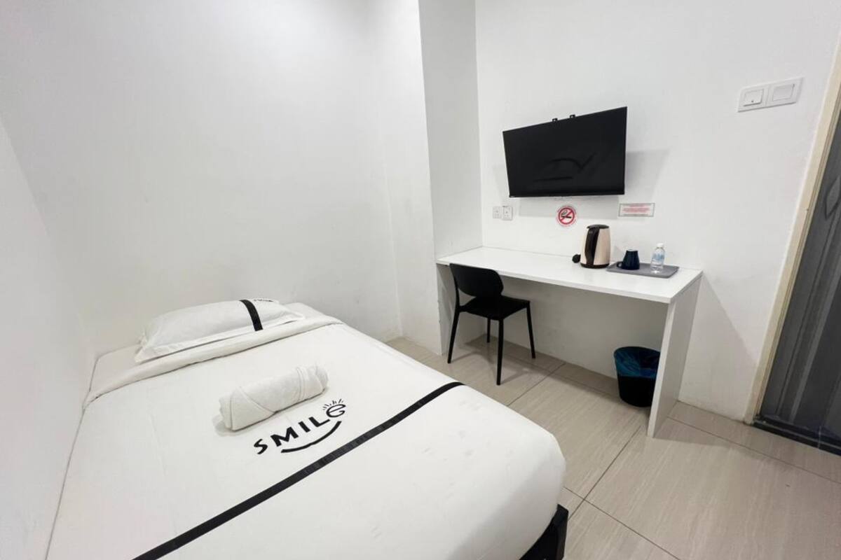 Une chambre d’hôtel équipée d’un lit, d’un bureau, d’une chaise, d’une télévision et d’une poubelle.
