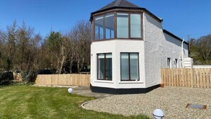 Ein modernes Haus mit einem großen Erkerfenster, einem umzäunten Garten und einer Auffahrt mit Kies.