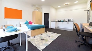 A compact room with a bed, a desk, a chair, a kitchenette, and a bathroom. - Raymont Hall (London)